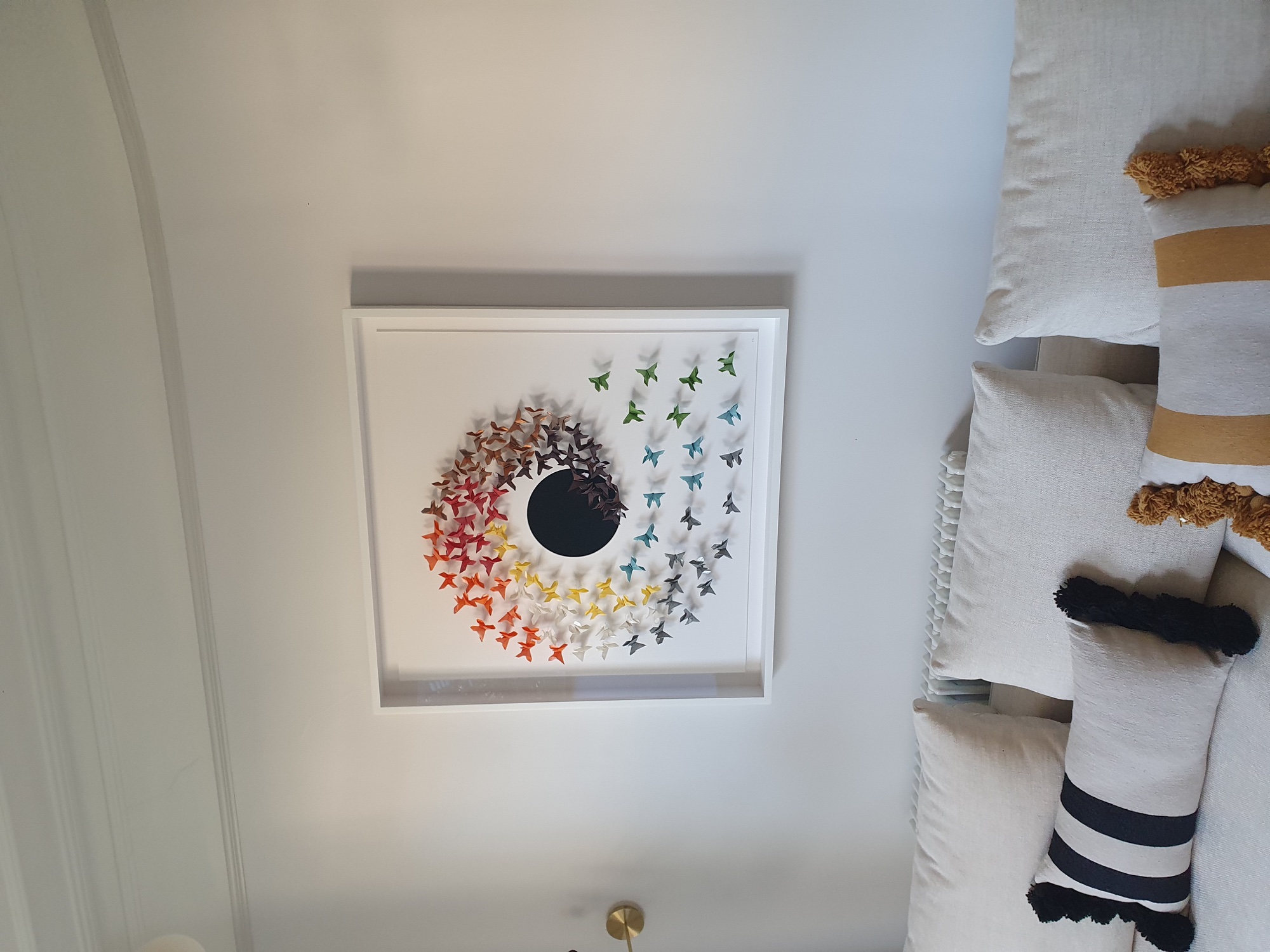 Multi-coloured origami butterfly artwork hanging above a sofa.